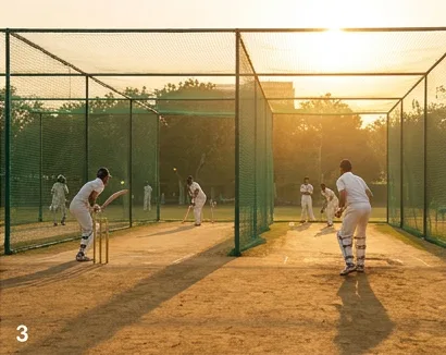 Cricketers practising inside professional net enclosures at sunset